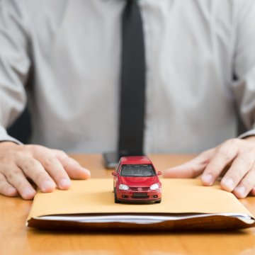 usaa extended vehicle protection service man with black tie on a desk holding paper folder and red toy car above it